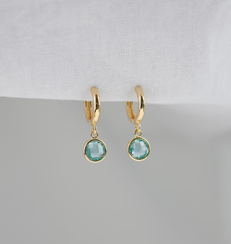 Pode incluir: Brincos de argola de ouro com uma gema azul claro pendurada.