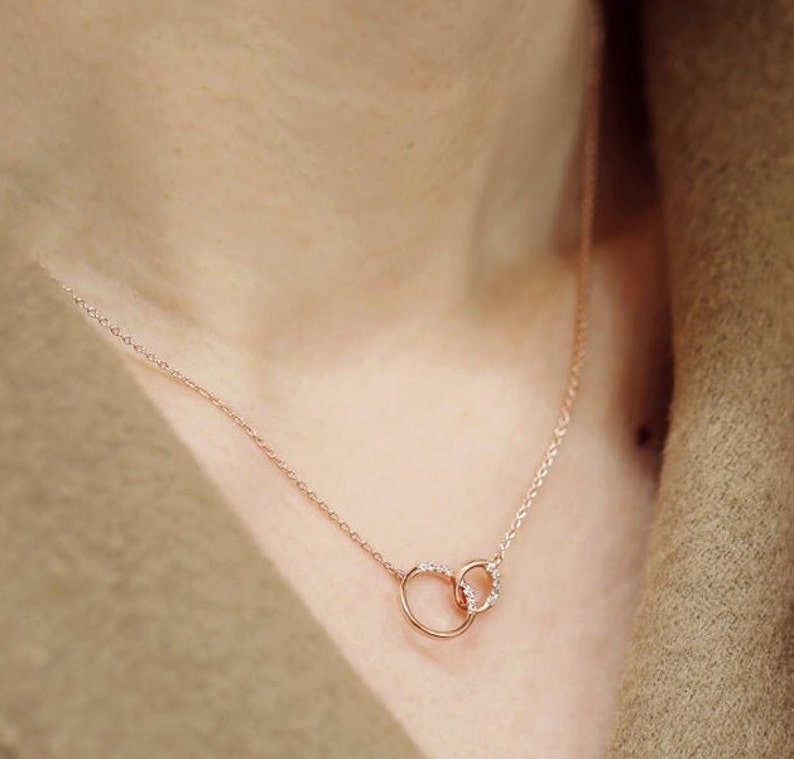 May include: A delicate rose gold necklace with two interlocking circles, each adorned with small sparkling diamonds.