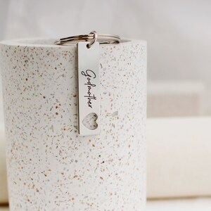 May include: Silver keychain with a rectangular tag that says "Godmother" with a heart cut out of the tag.