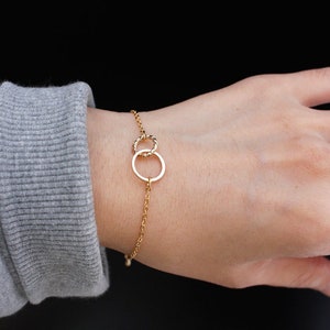 May include: A gold chain bracelet with two interlocking circles as a pendant.