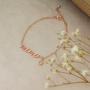 Op de afbeelding: Een ros&eacute;gouden armband met het woord "mimi" in cursief schrift en een kleine, heldere kristallen bedel.