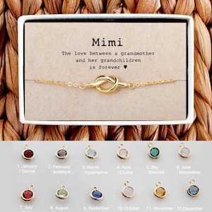May include: A gold knot bracelet with a card that reads "Mimi The love between a grandmother and her grandchildren is forever." The card is surrounded by twelve small round gemstones representing each month of the year.