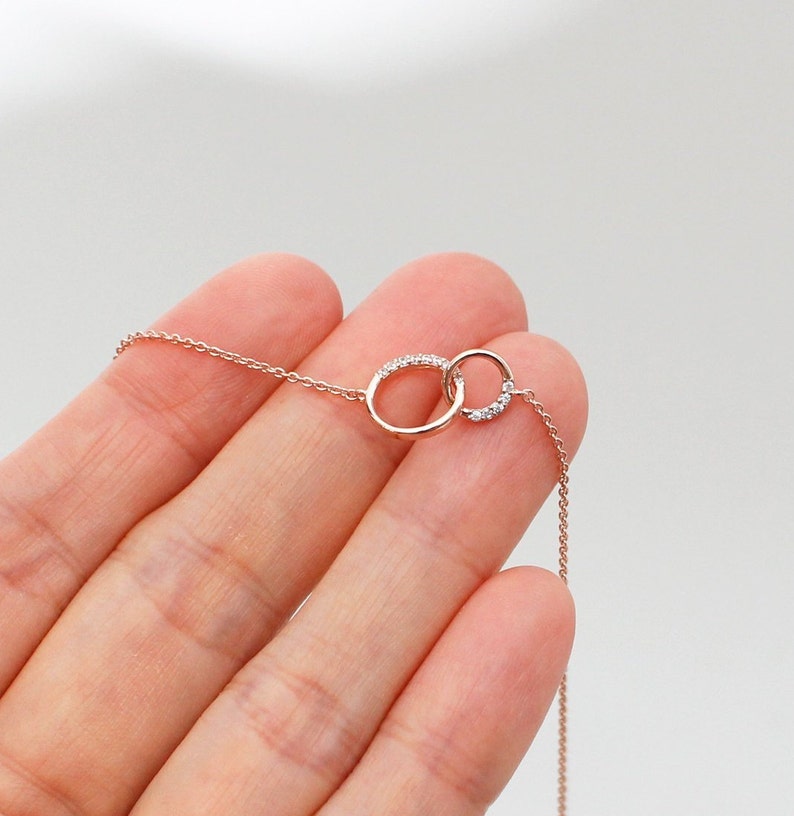 May include: A delicate rose gold necklace with two interlocking circles adorned with small sparkling diamonds.