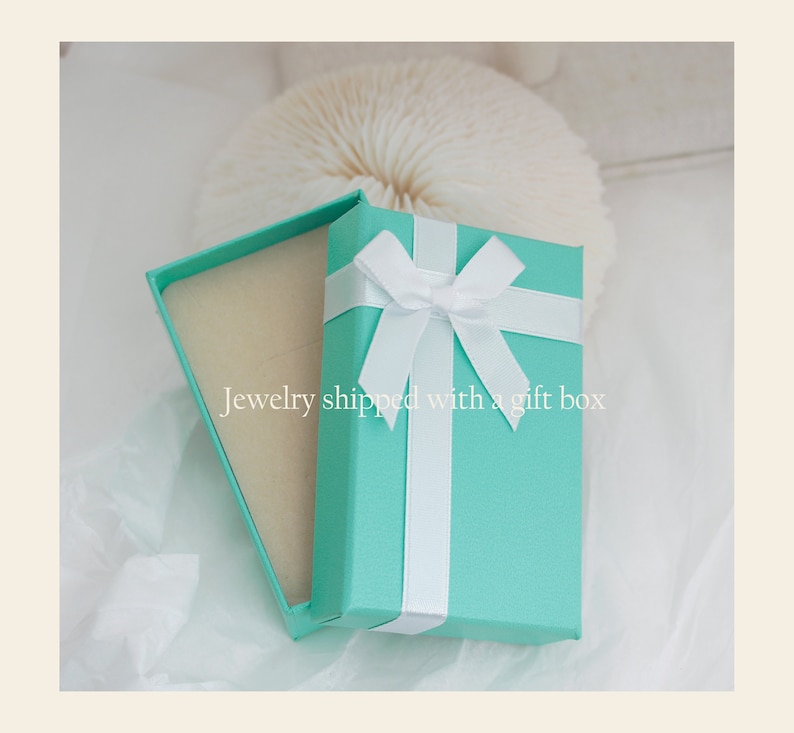 Puede incluir: Una caja de regalo turquesa con una cinta y un lazo blancos. La caja est&aacute; abierta y el interior est&aacute; forrado con papel de seda blanco. "Jewelry shipped with a gift box" est&aacute; escrito en el papel de seda.