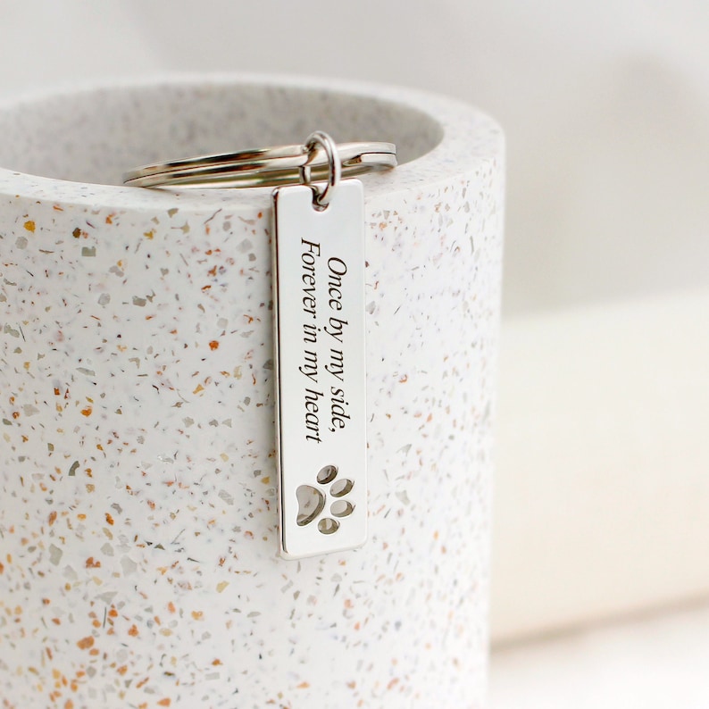 May include: Silver keychain with a rectangular tag that reads "Once by my side, Forever in my heart" with a paw print cutout.