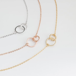 May include: Three delicate gold necklaces with interlocking circle pendants. The necklaces are in silver, rose gold, and gold.