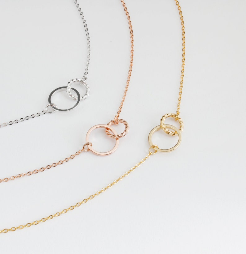 May include: Three delicate gold necklaces with interlocking circle pendants. The necklaces are in silver, rose gold, and gold.