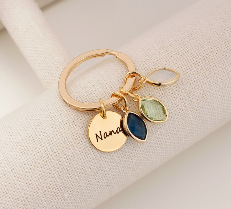 A gold O shaped keychain with coins and boat shaped birthstones. Personalized text, nana engraved on the coin. 
Customers can personalize birthstones and engraving for their grandmother. The most common comments are cute, pretty and high quality!