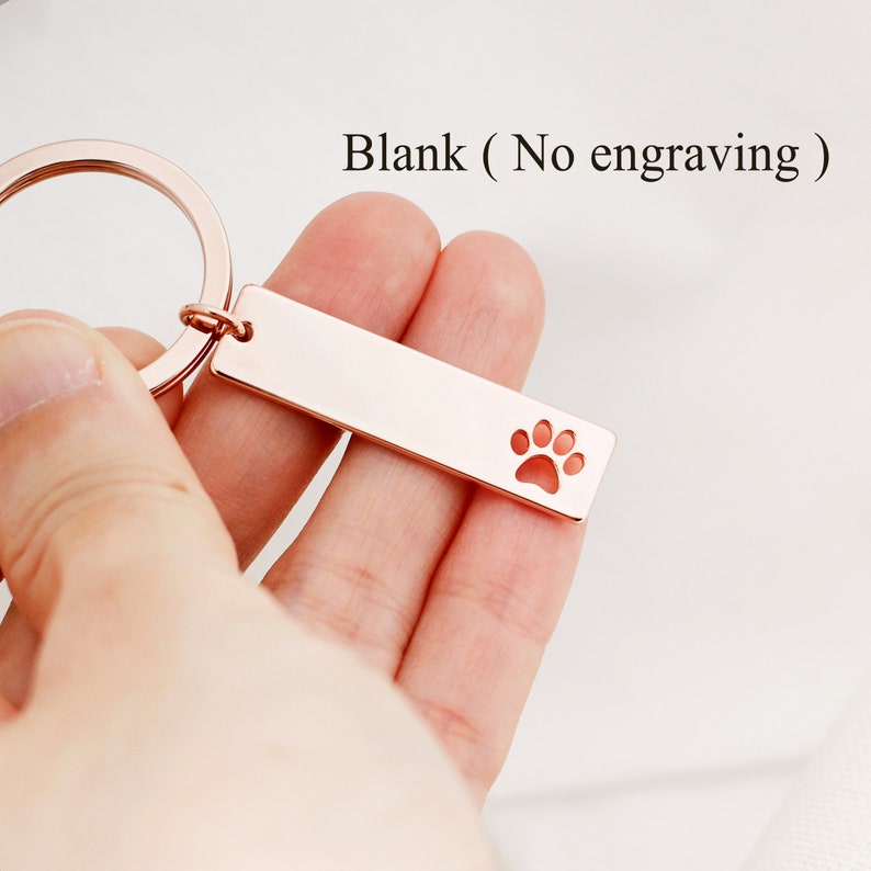 May include: Rose gold metal keychain with a paw print cutout. The keychain is blank, with no engraving.