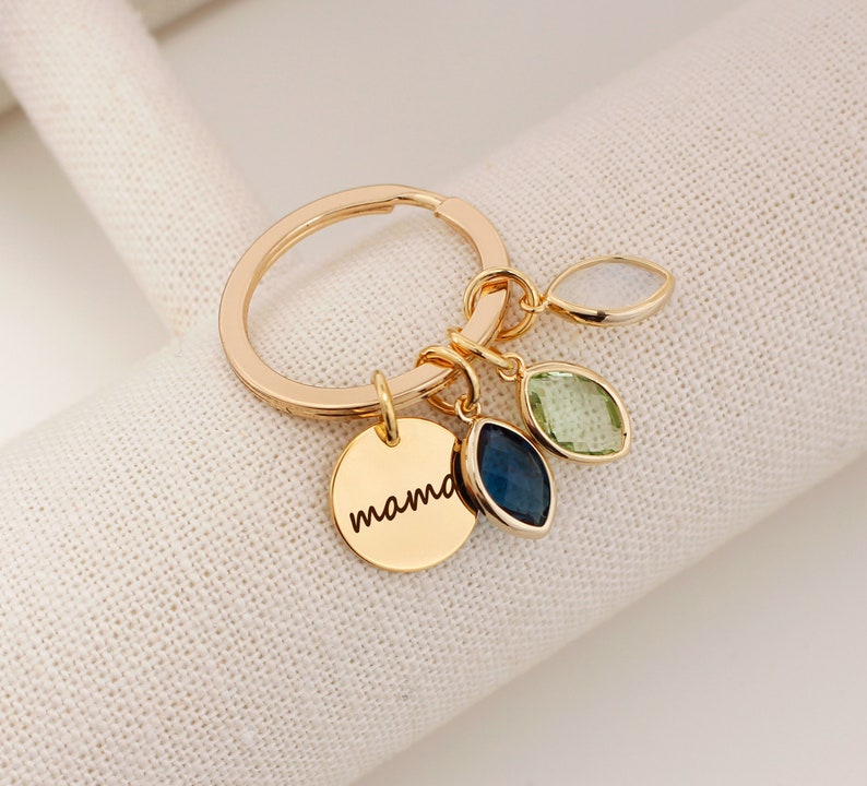 A gold O shaped keychain with coins and boat shaped birthstone Personalized text, mama engraved on the coin. Customers can personalize birthstones and engraving 
for their mother. The most common comments are cute, pretty and high quality!