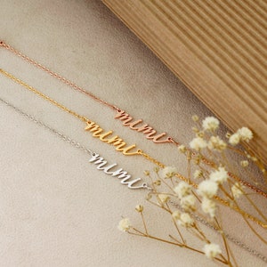 Op de afbeelding: Drie delicate gouden, ros&eacute;gouden en zilveren kettingarmbanden met het woord "mimi" in cursief op elk.