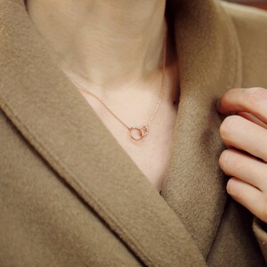 May include: A delicate rose gold necklace with two interlocking circles adorned with small sparkling diamonds.