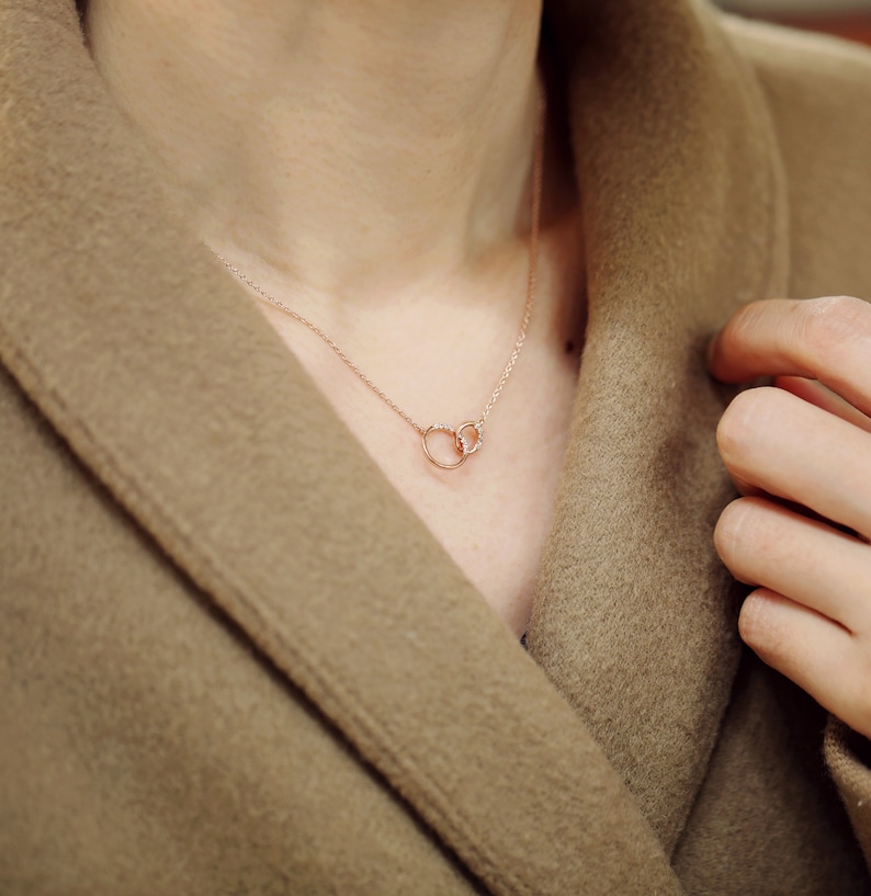 May include: A delicate rose gold necklace with two interlocking circles adorned with small sparkling diamonds.