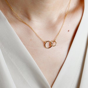 May include: A gold necklace with two interlocking circles. The smaller circle is twisted and the larger circle is smooth.