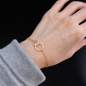 May include: A gold chain bracelet with a double circle charm. The chain is delicate and the circles are intertwined.