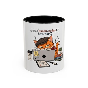 May include: A white ceramic mug with a black interior and rim featuring a graphic of an orange tabby cat wearing a flat cap, working on a laptop. The text reads while (human.codes) { cat.nap(); } with a to-do list, coffee cup, and books.