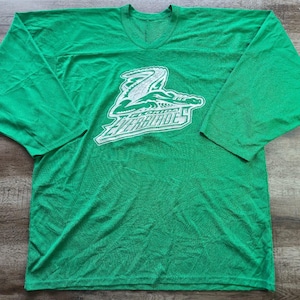 May include: A bright green long-sleeve jersey featuring a white graphic of an alligator and the text Florida Everblades printed on the chest. The garment has a V-neck collar and wide sleeves, showcasing a sports-inspired design with a bold color.