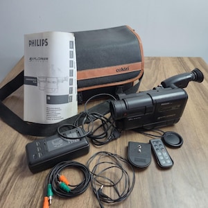 Pode incluir: Uma câmara de vídeo Philips Explorer preta com lente de zoom digital 24x, acompanhada por um saco de transporte Cokin, manual de instruções, carregador de bateria, controlo remoto, suporte para tripé e cabos de áudio e vídeo pretos.