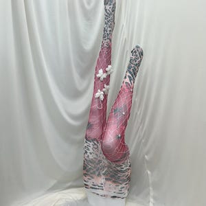 Puede incluir: Un par de medias estampadas en rosa y gris con una superposición de red. Las medias están adornadas con pequeñas mariposas de tela blanca y delicados detalles tipo perla sujetos a la malla, creando una apariencia texturizada y en capas.
