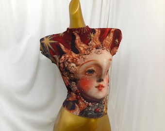 May include: A short-sleeved, pleated top featuring a vibrant, multi-colored graphic print of a stylized sun face with golden rays, red accents, and star motifs against a deep red background, worn on a gold-colored mannequin torso.