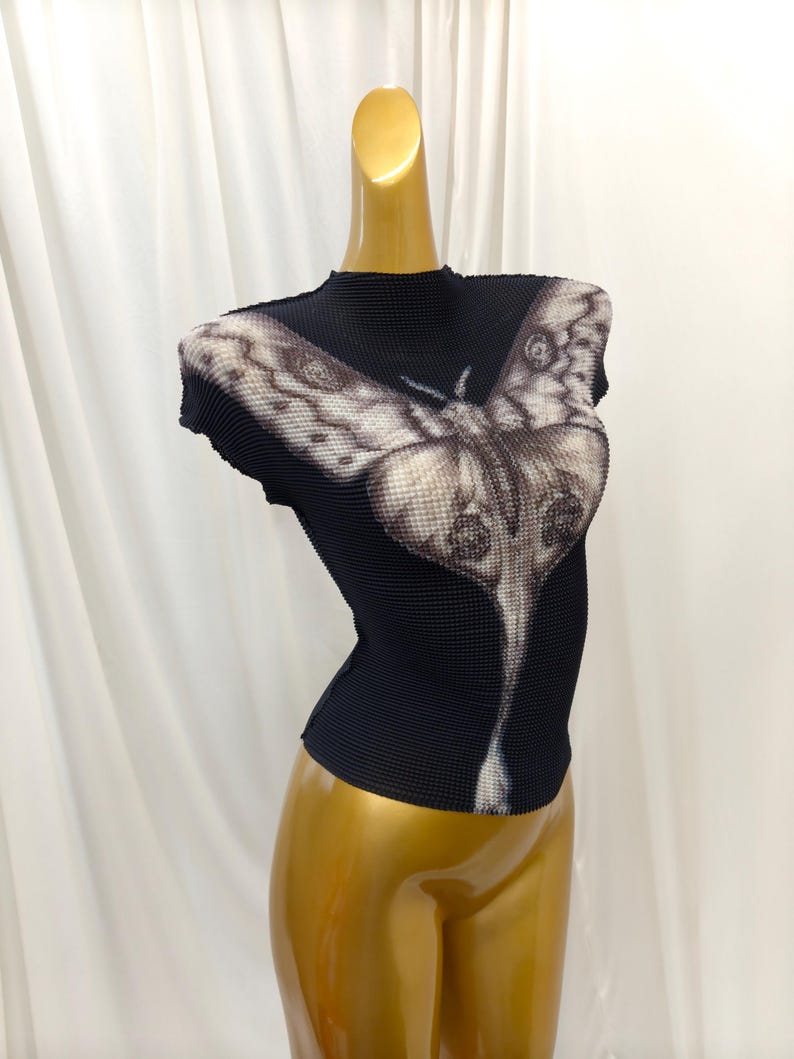 May include: A black short-sleeved top with a high neckline and a textured, pleated fabric surface. The front features a large, detailed graphic print of a moth in shades of white, gray, and black, extending from the chest down to the waist.