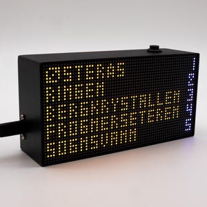 May include: A rectangular black electronic display board with a dot matrix screen showing yellow text that reads OSTERAS, RINGEN, BERGKRYSTALLEN, FROGNERSETEREN, SOGNSVANN, and a vertical column of blue numbers 1 through 5 on the right side.