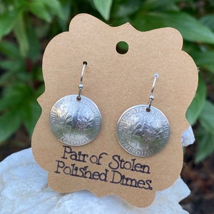 May include: A pair of silver earrings made from polished US dimes. The earrings are hanging from a brown card with the text "Pair of Stolen Polished Dimes".