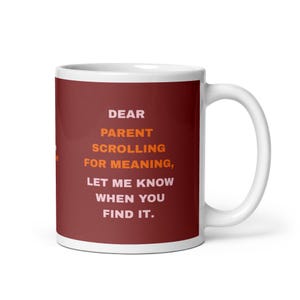 Op de afbeelding: Een witte keramische mok met een donkerrode buitenkant met de tekst in lichtroze en oranje: DEAR PARENT SCROLLING FOR MEANING, LET ME KNOW WHEN YOU FIND IT. De mok heeft een standaard handvat aan de rechterkant en een gladde afwerking.