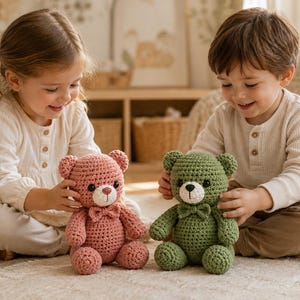 Puede incluir: Dos osos de peluche tejidos a ganchillo a mano, uno de color rosa empolvado y el otro de color verde salvia. Cada oso presenta una pequeña pajarita a juego en el cuello, un hocico blanco y ojos de seguridad oscuros. Los osos están sentados.