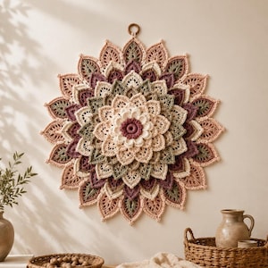 May include: A circular crochet wall hanging featuring a layered, petal-like design in shades of cream, sage green, and deep plum. The intricate, multi-tiered floral pattern radiates from a central point, finished with a small wooden hanging ring.