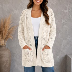 Può includere: Un cardigan aperto color bianco sporco con un motivo a maglia larga e testurizzata, maniche lunghe e due tasche frontali applicate. Il capo presenta bordi a coste lungo il colletto, i polsini e l'orlo, offrendo una finitura strutturata.