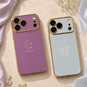 May include: Two rectangular smartphone cases with gold-toned metallic edges and camera surrounds. The left case is purple with a white crescent moon, a small star, and the text LUNA. The right case is light blue with a white butterfly and the text SKYE.
