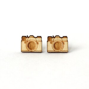 Op de afbeelding: Een paar houten camera-oorbellen. De oorbellen zijn gemaakt van lichtbruin hout en hebben een eenvoudig camera-ontwerp.
