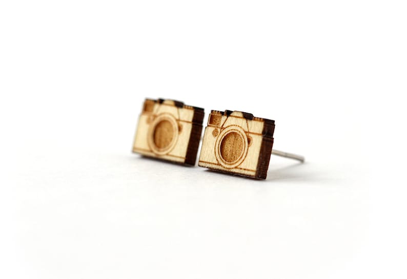 Op de afbeelding: Een paar houten camera-oorbellen. De oorbellen zijn gemaakt van lichtbruin hout en hebben een eenvoudig camera-ontwerp.