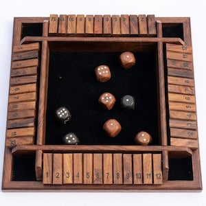 May include: A square wooden board game with a black felt center and four sides featuring hinged wooden tiles numbered one through twelve. Six dice, including four brown wooden dice and two black dice with white pips, are scattered on the felt.