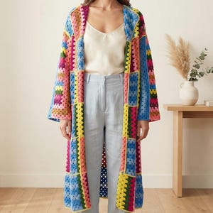 May include: A long, open-front cardigan made from multi-colored granny square crochet patches. The garment features a vibrant palette of blue, yellow, pink, green, and purple yarn, with long sleeves and a straight, knee-length silhouette.