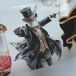 Pode incluir: Um autocolante com a ilustração de um coelho branco vestido com um fraque preto, uma cartola com uma faixa dourada e um colete com padrão dourado. O coelho usa uma gravata borboleta e luvas, apontando com uma mão numa pose dinâmica.