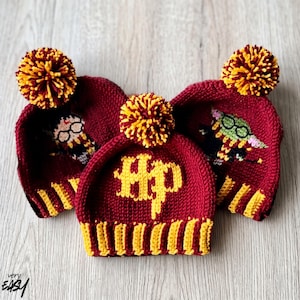 Pode incluir: Três gorros de malha bordô e amarelos com pompons. O gorro central apresenta as letras amarelas HP. O gorro esquerdo mostra uma personagem com óculos e o direito uma personagem verde com óculos, ambos com um padrão de malha.