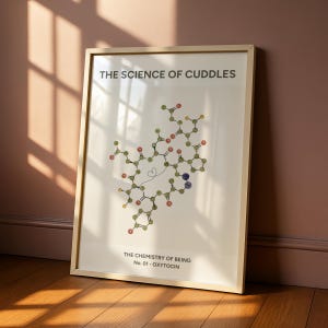 May include: A framed wall art print featuring a molecular structure diagram in green, red, and blue circles. The text reads THE SCIENCE OF CUDDLES at the top and THE CHEMISTRY OF BEING No. 01 - OXYTOCIN at the bottom on a light cream background.