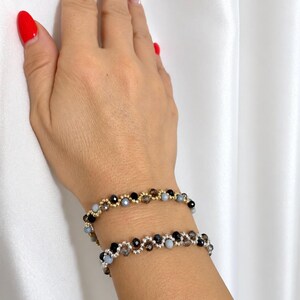 Può includere: Due braccialetti di perline caratterizzati da un motivo ondulato e interconnesso di piccole perline rotonde. Un braccialetto è realizzato con distanziatori color oro, mentre l'altro utilizza distanziatori color argento. Entrambi incorporano perline nere, grigie e traslucide.