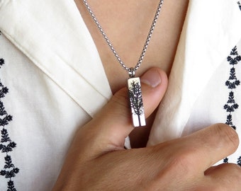 May include: A silver chain necklace with a rectangular pendant featuring a detailed tree design.