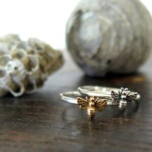 May include: Two silver rings with bee charms. The bee on the left ring is gold, and the bee on the right ring is silver.
