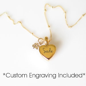 May include: Gold heart-shaped pendant necklace with a small paw print charm. The heart is engraved with the name "Sadie". Custom engraving is included.