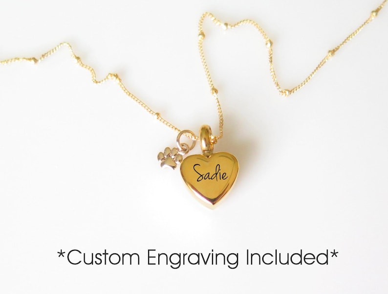 May include: Gold heart-shaped pendant necklace with a small paw print charm. The heart is engraved with the name "Sadie". Custom engraving is included.