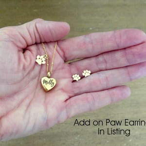 May include: Gold necklace with a heart pendant engraved with the name "Molly" and a paw print charm. Matching gold paw print earrings are also shown.