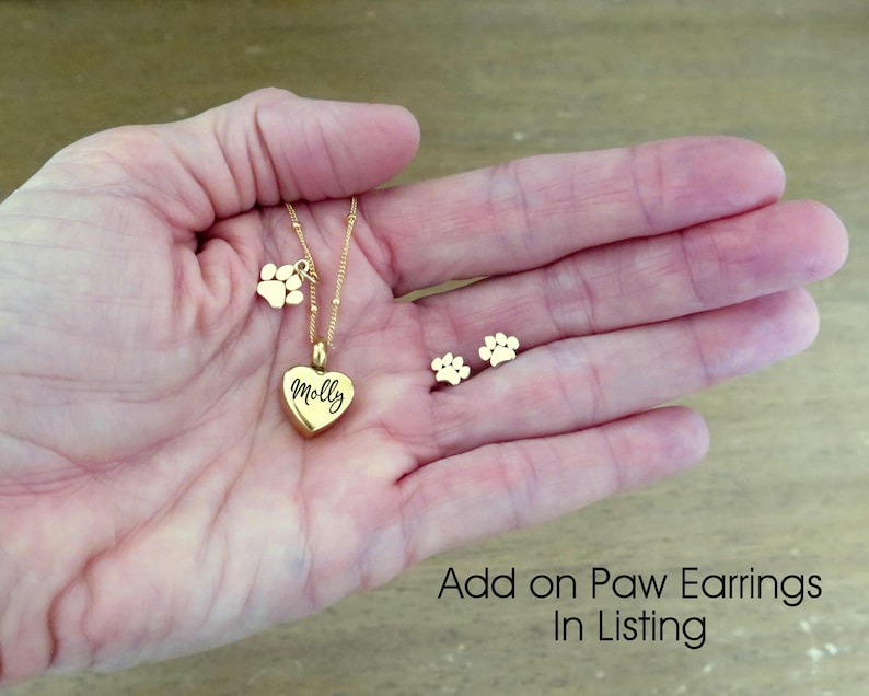 May include: Gold necklace with a heart pendant engraved with the name "Molly" and a paw print charm. Matching gold paw print earrings are also shown.