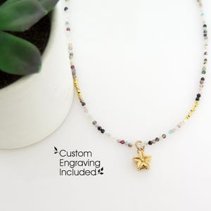 May include: A delicate necklace featuring small, multi-coloured gemstone beads interspersed with gold-toned accents and a central gold-toned star charm. The text "Custom Engraving Included" is printed in black near the bottom left of the image.