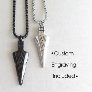 May include: Two silver necklaces with arrowhead pendants. The arrowheads have a geometric pattern and are black and silver. The text "Custom Engraving Included" is printed below the necklaces.