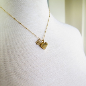 May include: Gold necklace featuring a heart-shaped pendant engraved with the name "Bella" and a small paw print charm.