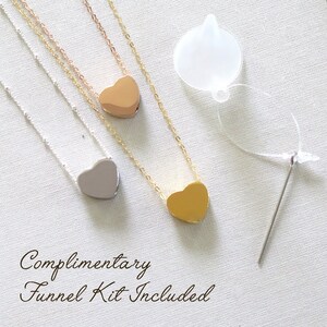 May include: Three silver, gold, and rose gold heart necklaces with a complimentary funnel kit for filling the heart pendants. The kit includes a clear plastic funnel and a needle.